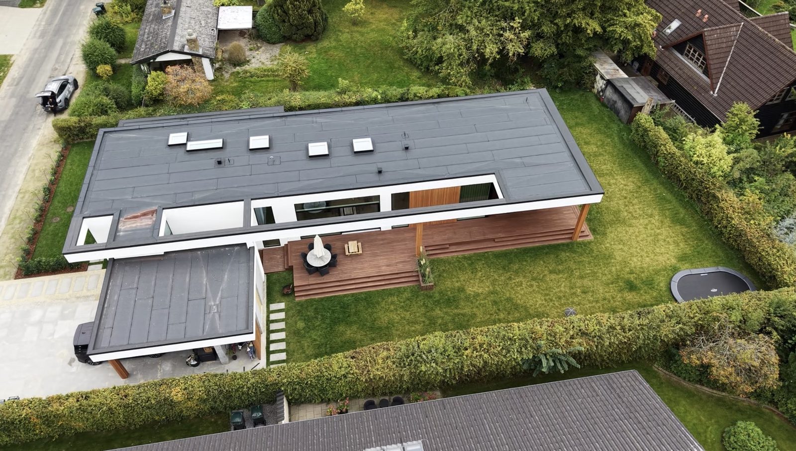 Dronefoto oppefra af moderne villa med fladt tag, ovenlysvinduer og stor træterrasse